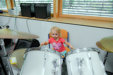 A little girl tries to play the drum kit at a music school.