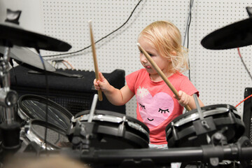 Obraz na płótnie Canvas A little girl plays drums and percussion instruments at a music school.