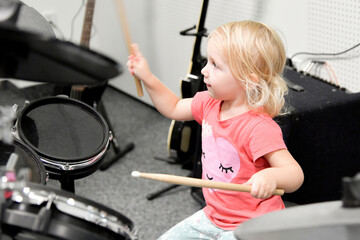 A little girl tries to play the drum kit at a music school.