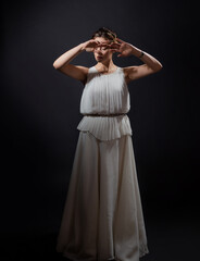 Fototapeta premium An ancient heroine, a young woman in the image of an ancient Greek goddess or muse. A noble heroine in a white tunic and a laurel wreath, dancing on a black background