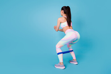 Full length back view photo of pretty chinese woman use rubber expander dressed trendy sporty look isolated on bright blue color background