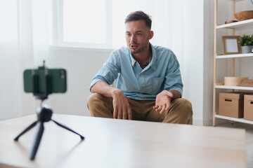Fototapeta premium Self-confident attractive influencer blogger record online webinar lesson for subscribers with phone at home table. Copy space. Electronic IT PC accessories Gadget addiction Online education concept