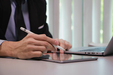 a young businessman using a digital tablet and digital pen, working hard with a laptop computer in the modern office
