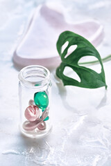 Various serum capsules for healthy skin routine. Anti-wrinkle rejuvenation skin treatment. Beauty product presentation. Off white stone marble background with monstera leaf.