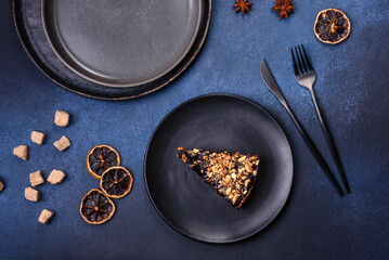 A piece of fresh delicious cake with nuts and chocolate on a black plate against a dark blue background