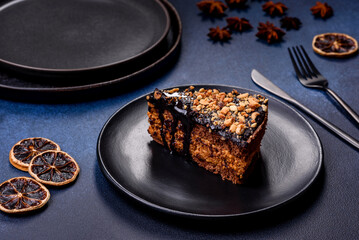 A piece of fresh delicious cake with nuts and chocolate on a black plate against a dark blue...