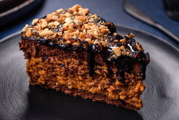 A piece of fresh delicious cake with nuts and chocolate on a black plate against a dark blue background