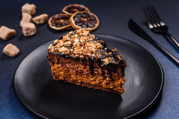 A piece of fresh delicious cake with nuts and chocolate on a black plate against a dark blue background