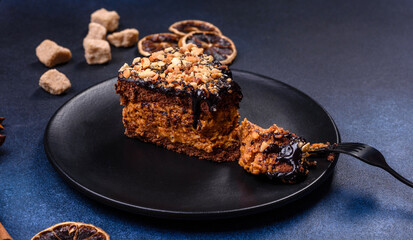 A piece of fresh delicious cake with nuts and chocolate on a black plate against a dark blue background