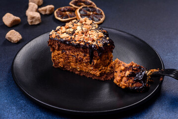 A piece of fresh delicious cake with nuts and chocolate on a black plate against a dark blue background