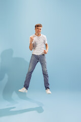 Portrait of young man in casual clothes cheerfully jumping, posing isolated over blue studio background. Success and happiness