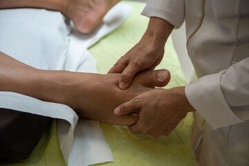 Um profissional fazendo massagem terapêutica no pé do paciente que está deitado na maca. - obrazy, fototapety, plakaty