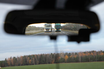 Two trucks overtaking in rear mirror view on highway at autumn morning