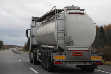 Old semi truck food barrel move on suburban highway road at autumn evening in perspective, back view, Liquid food production cargo transportation logistics in Europe