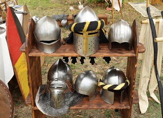 Six medieval knight helmets  on a wooden shelf.