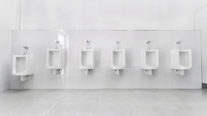 Men's room with white porcelain urinals in line. Modern clean public toilets with tiles . Comfort...