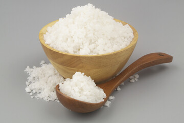Sea salt in wooden bowl and spoon on gray background