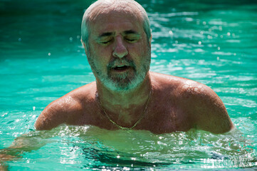senior man swimming in summer pool on summertime vacation