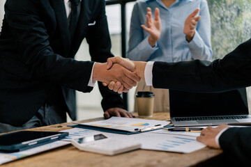 Close up of female and male shaking hands, businessman and businesswoman handshaking at office table with charts graphs after successful negotiations, partners concluding contract