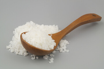 Sea salt in wooden spoon and on gray background