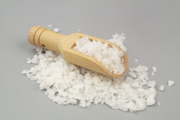 Heap of coarse sea salt with wooden scoop on gray background