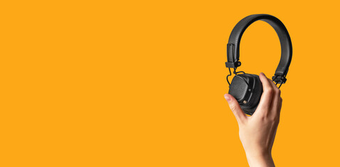 Banner with hands holding headphones on orange background. Listening to music, audiobooks, relax, entertainment concept. Accessories for leisure, study. Copy space