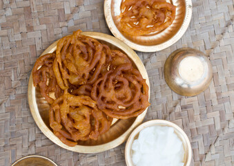 Popular Indian Sweet Dish or Dessert called Jalebi or imarti soaked in sugar syrup presented in copper or brass plate. Festival Food. Selective Focus on Subject, Background Blur