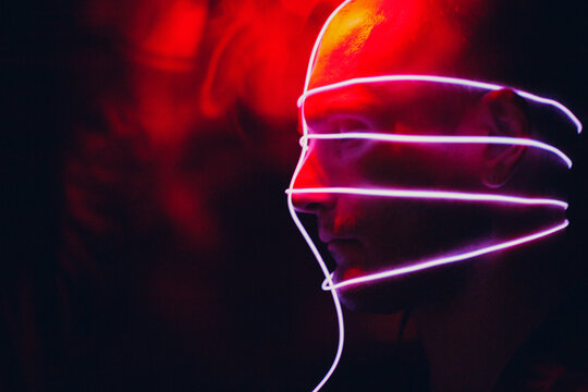 Portrait Of Man With Neon Glow Tube Lines On His Face In Dark. Concept Cyberpunk And Virtual Reality