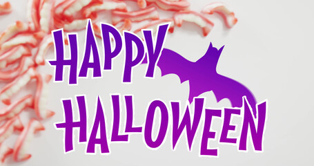 Happy halloween text banner with bat icon against halloween candies on grey surface