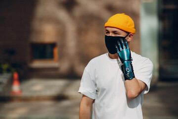 Young disabled man with artificial prosthetic hand wearing medical protective face mask