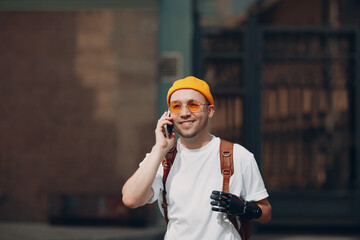 Young disabled man hold mobile phone artificial prosthetic hand in casual clothes and backpack...
