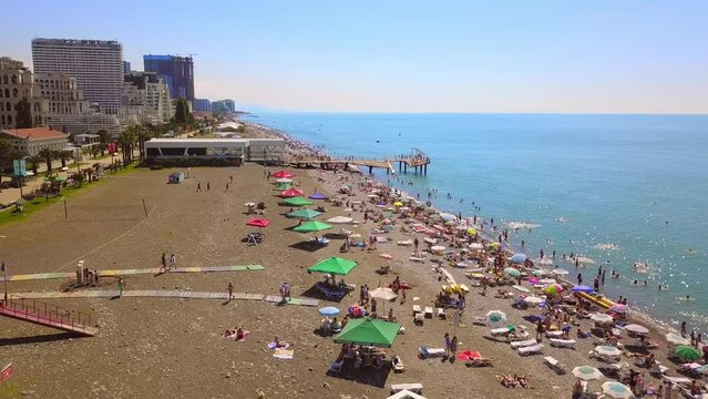 Aerial view on beach and umbrellas. Beach and blue water against backdrop of big city. Top view from drone at beach and azure sea. View of beach with colorful umbrellas, bathing people in water