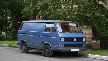 An old blue minibus is parked near the lawn, Kollontai Street, St. Petersburg, Russia, August 2022