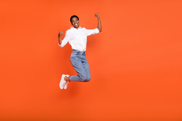 Full size photo of overjoyed positive female jumping raise fists in success triumph isolated on orange color background