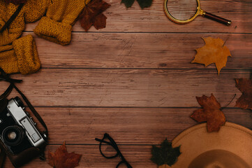 Frame of autumn accessories, flatlay. Hat, sweater, leaves maple, glasses, retro camera on wooden background. Copying space