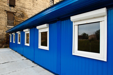 Construction change house fragment. Temporary blue building for builders. Portable blue change house. Long construction building next to brick wall. Concept of selling change houses for builders