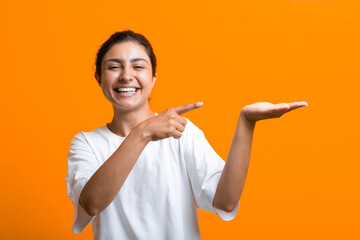 Portrait of young smiling adult indian woman with empty hand palm showing holding something advertising template