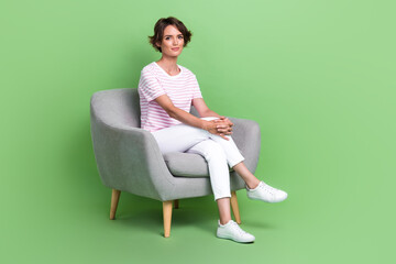 Fototapeta na wymiar Full body photo of charming young lady sit soft armchair hr job interview dressed trendy striped clothes isolated on green color background