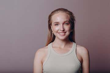 Portrait of young smiling european woman. Beautiful happy blonde girl wears t-shirt and looks at camera. Studio shoot isolated on pink background.