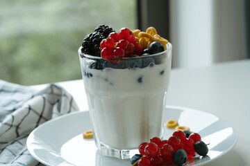 Yogurt, breakfast loops oat cereal, and fresh summer berries  in glass on white table