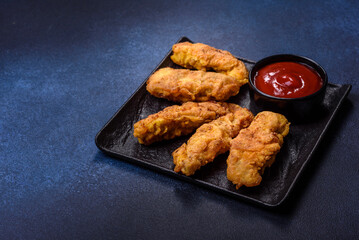 Fried crispy chicken nuggets with ketchup on black plate on a dark background