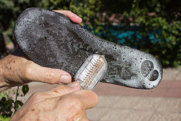 Hands brushing a shoe insole with soap and bubbles outside in broad daylight.
