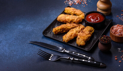 Fried crispy chicken nuggets with ketchup on black plate on a dark background