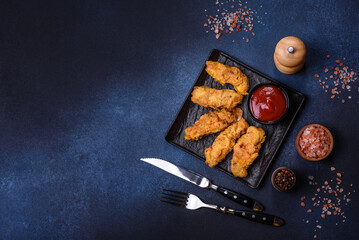 Fried crispy chicken nuggets with ketchup on black plate on a dark background