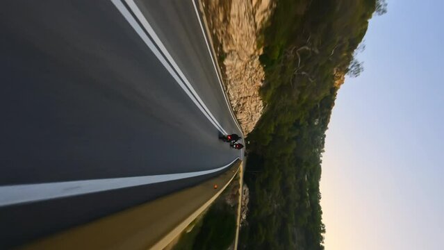 Two Motorcyclists driving on a serpentine road during golden sunrise, vertical