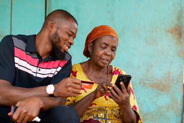 elderly african woman and young man use phone and credit card - obrazy, fototapety, plakaty