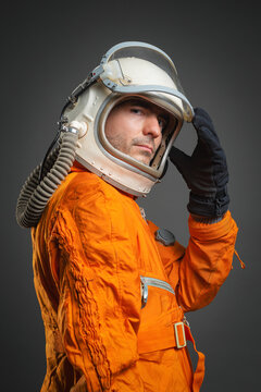 Serious astronaut is standing in the space suit and helmet on the gray background.