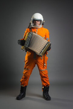 Astronaut in space suit and helmet is playing on the accordion on the gray background.