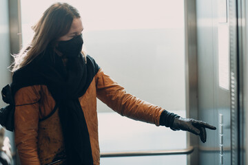 Woman in face medical mask with hand in glove forefinger pressing the button elevator during...