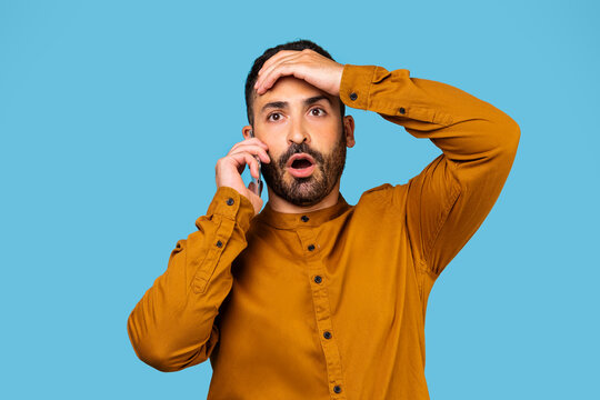 Bad news. Portrait of a shocked frightened caucasian man, receiving shocking news from a call with his mouth open, posing isolated on a blue studio background.
